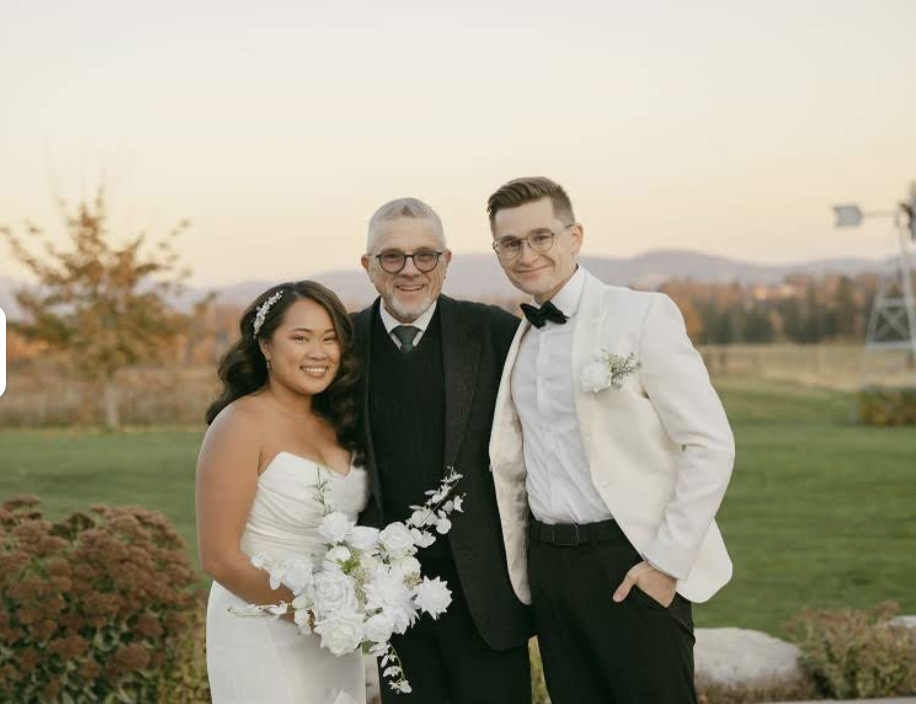 Wedding officiant from Celebrations by Stephen standing with a newly married couple after their outdoor ceremony at sunset, smiling together in a scenic field.